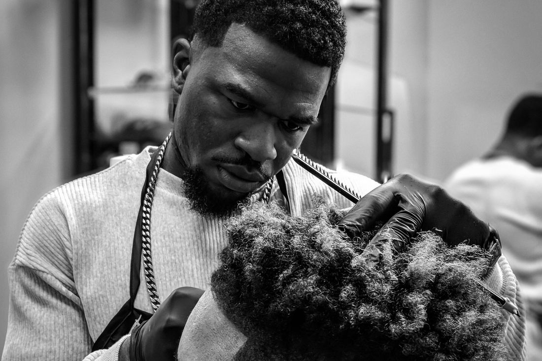 A barber concentrating as he cuts a client's curly hair with clippers