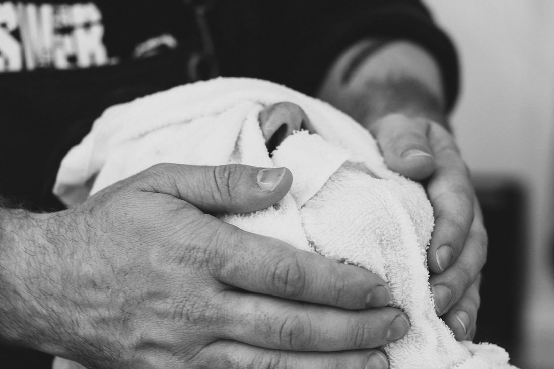 A barber's hands pressing a warm towel across a client's face