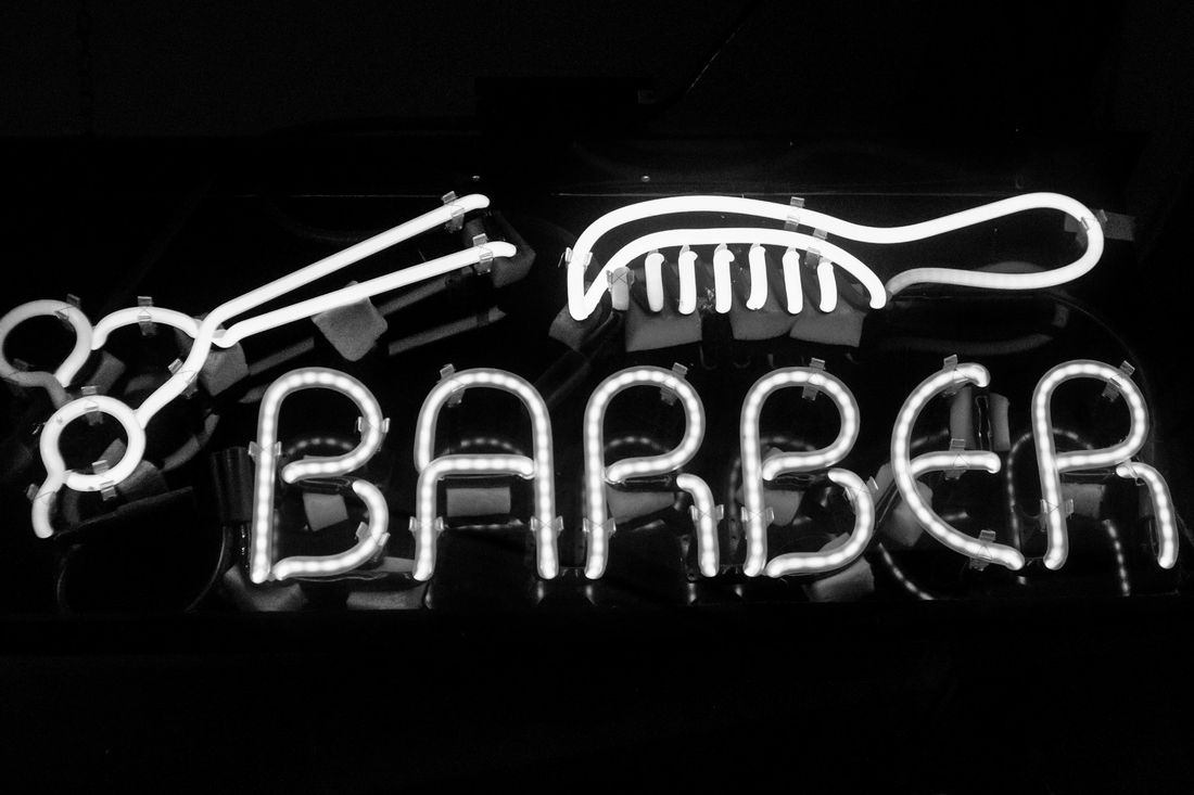 A glowing neon sign spelling BARBER with scissors and a comb