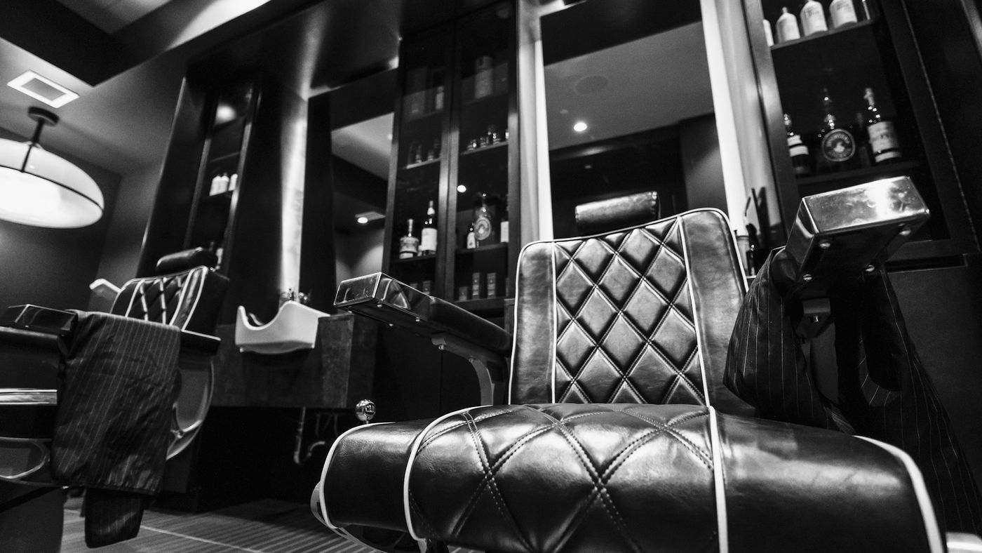 A dark, moody barbershop interior with a tufted leather chair and mirrors