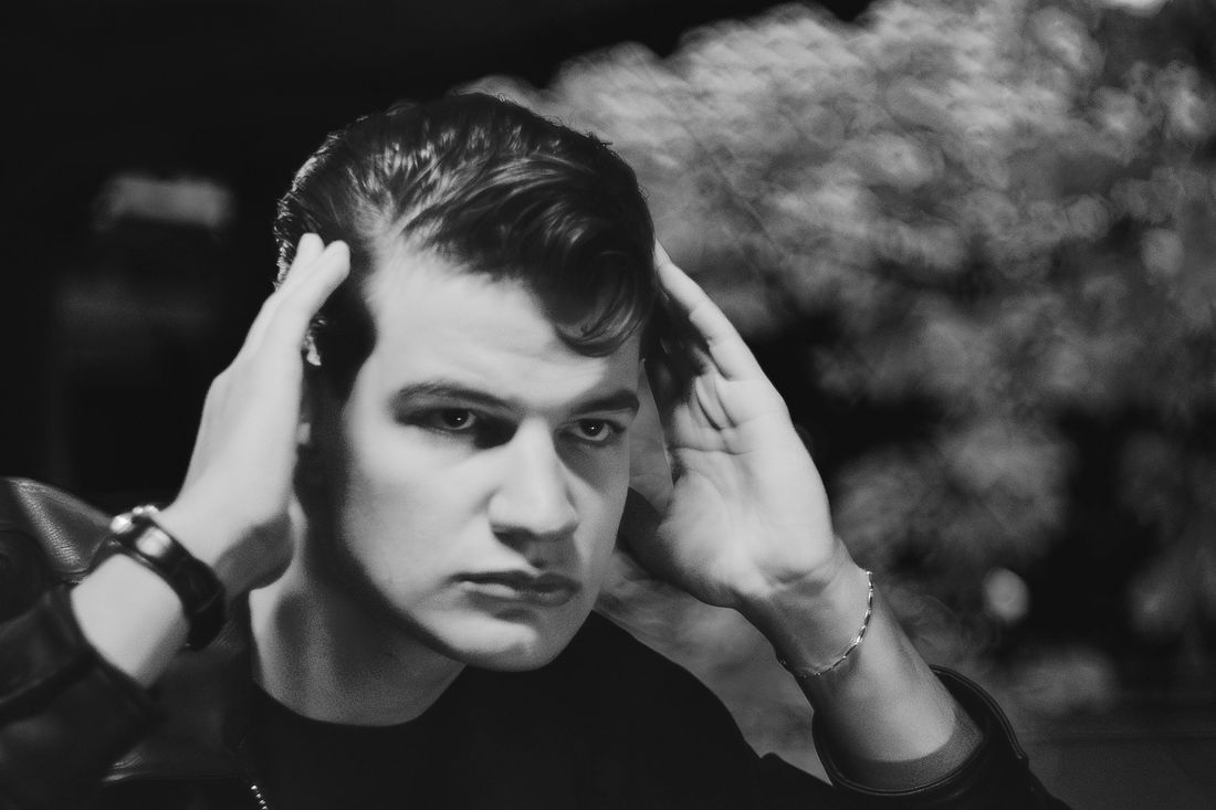A young man adjusting the front of his hair with both hands