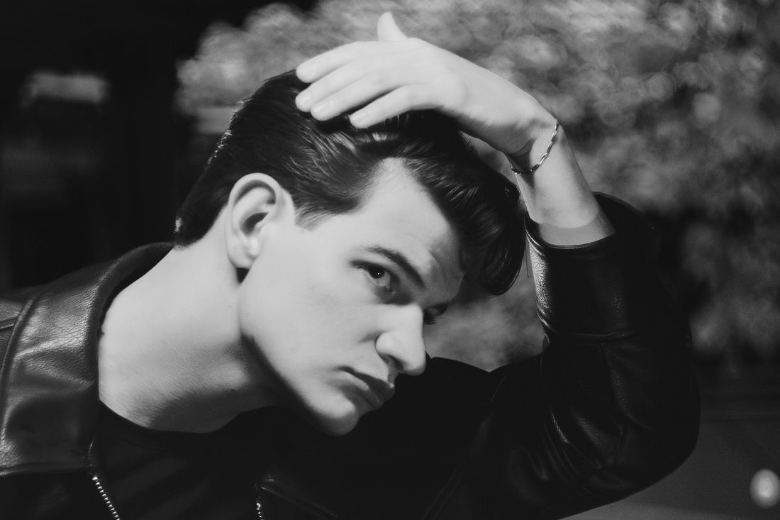 A young man in a leather jacket running a hand through his swept-back hair