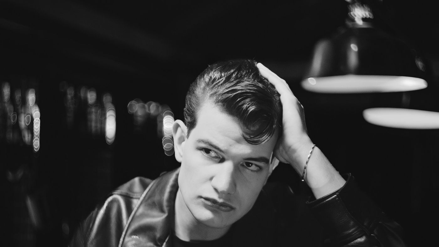 A young man in a leather jacket pushing his hair up and back