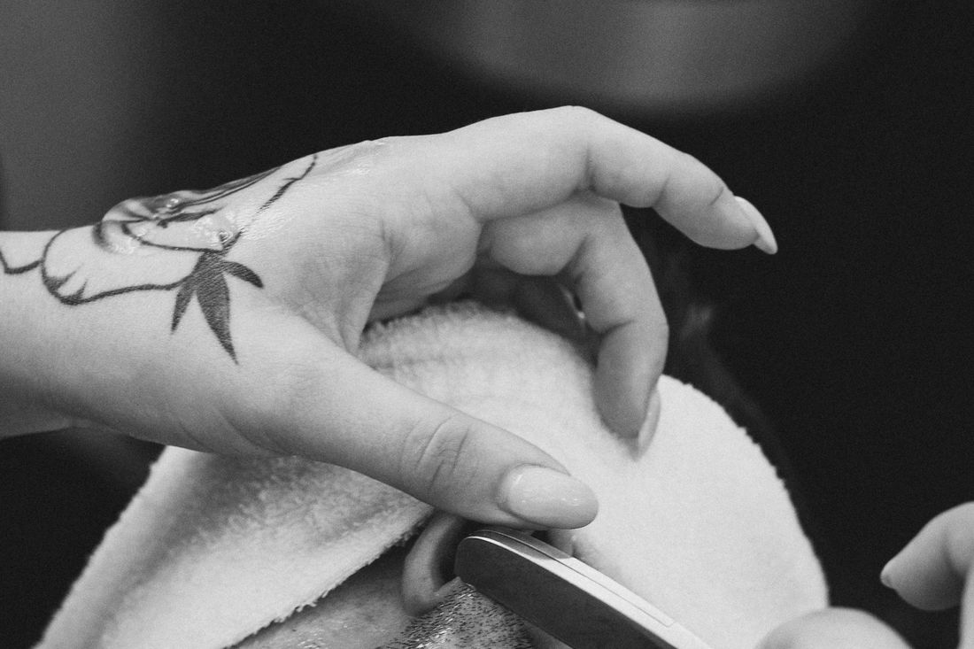 A barber's hand holding a straight razor beside a towel-wrapped client