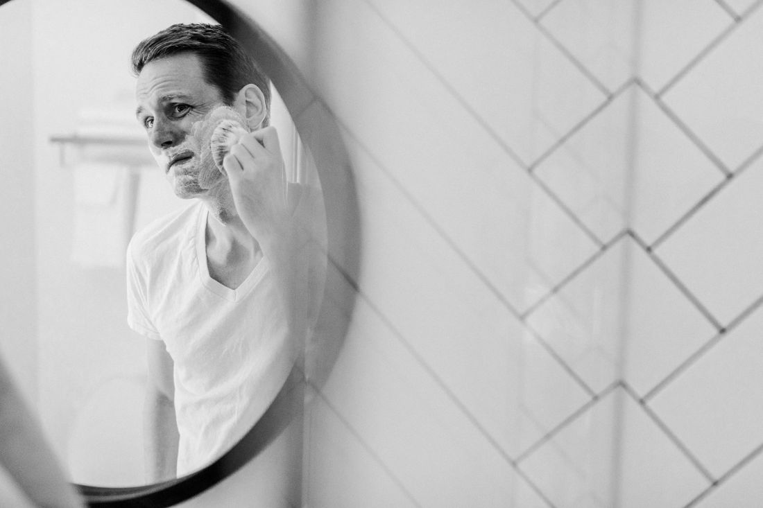 A man shaving in a round wall mirror