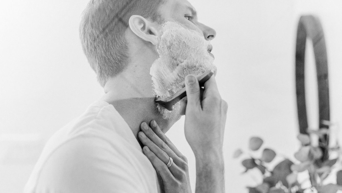 A man shaving lathered skin in front of a mirror