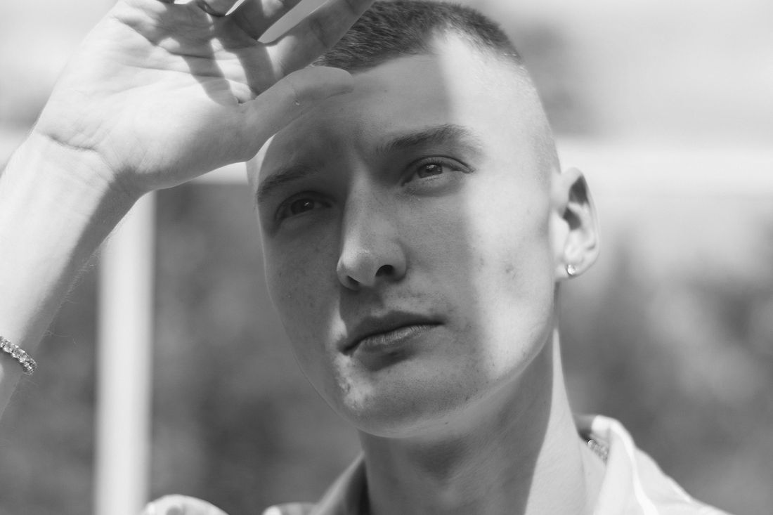 A man with short hair resting a hand on his forehead