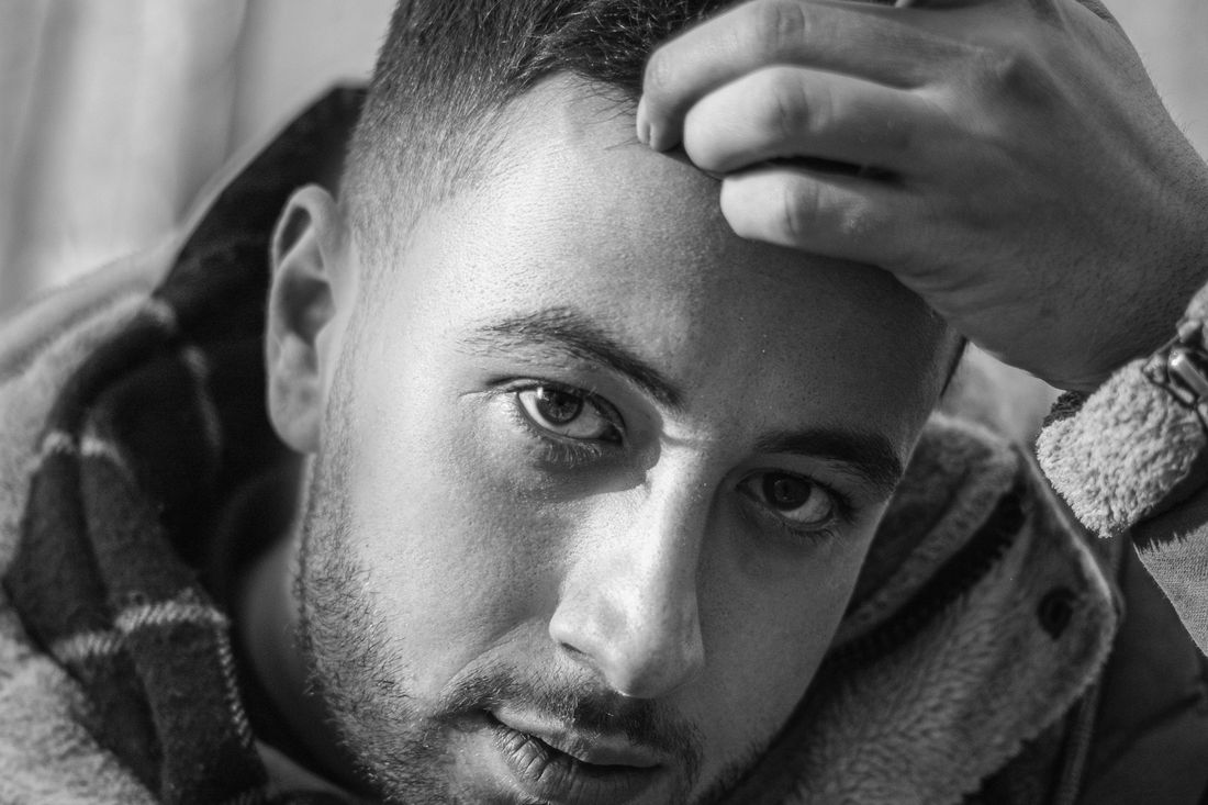 A young man with short sides running a hand through the top of his hair