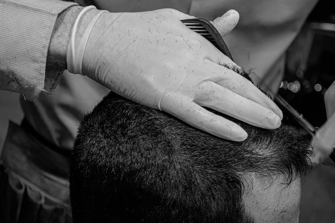 A gloved barber working carefully through a client's hair