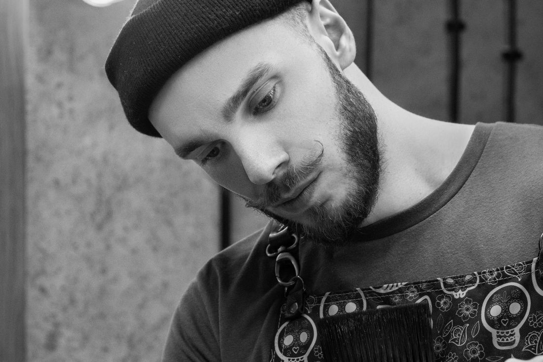 A young man in a beret with a short beard looking down