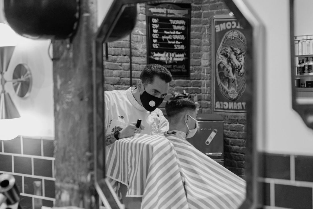 A client in a barber's cape seen in a barbershop mirror
