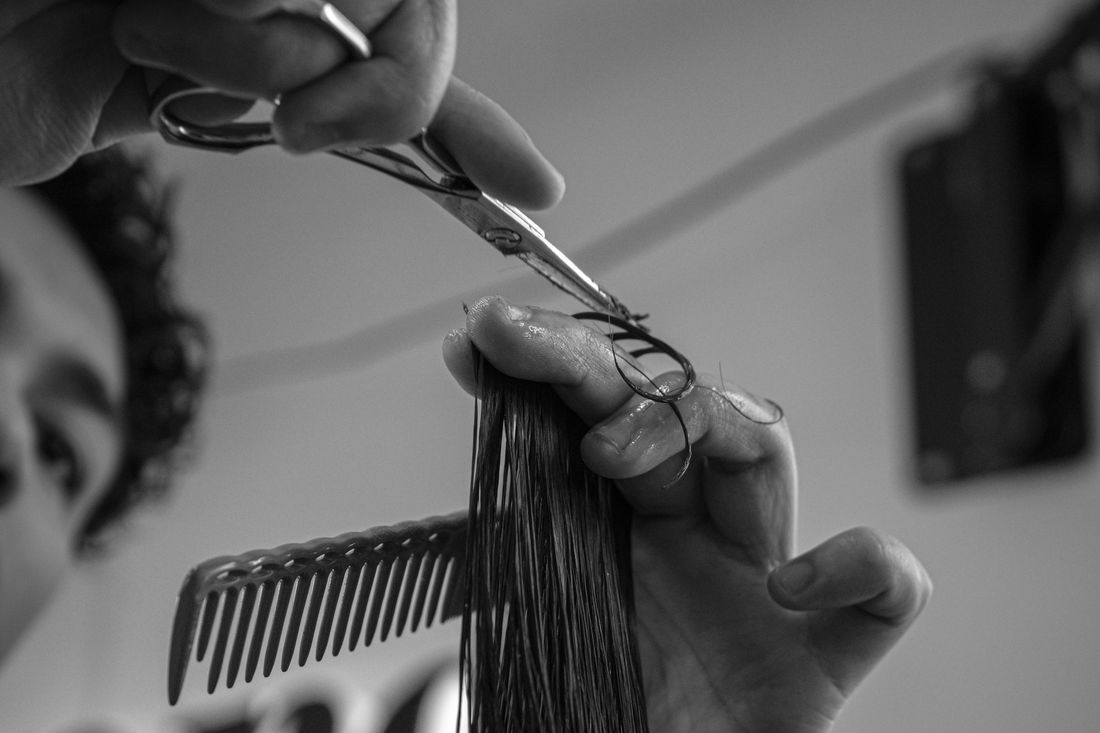 A barber lifting hair with a comb and cutting along it with scissors