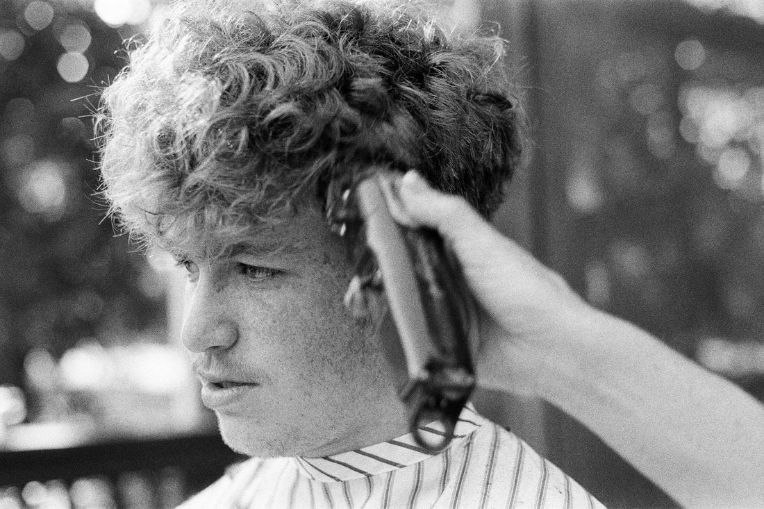 A barber running clippers through a young man's curly hair