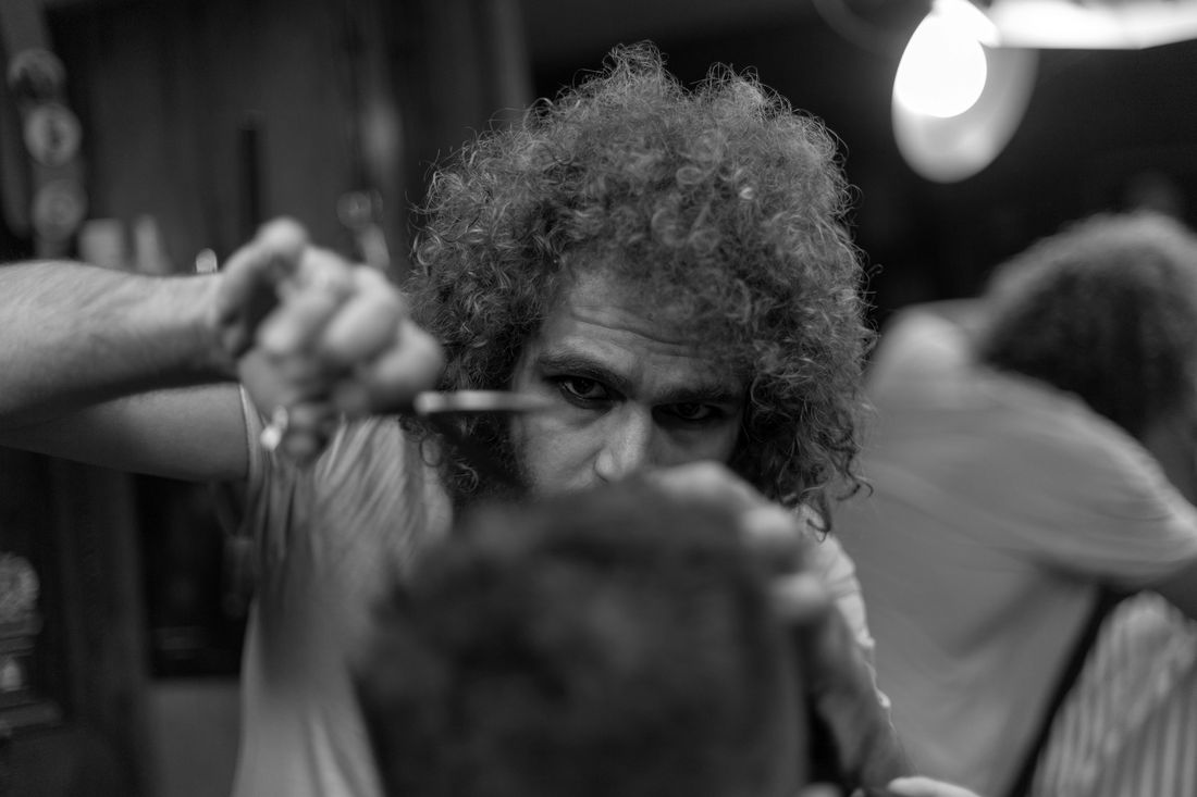 A barber cutting a client's thick curly hair with scissors