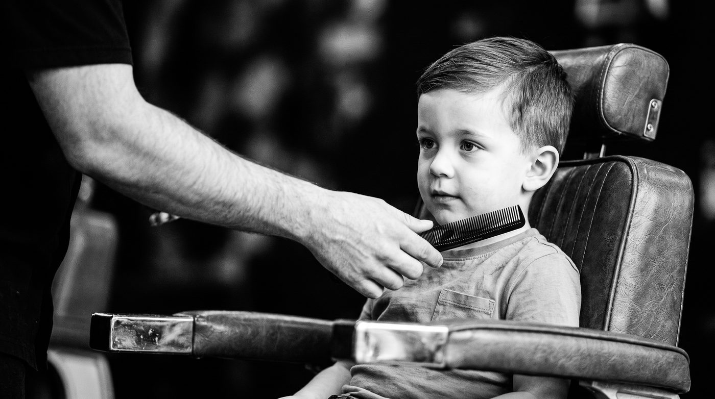 A barber’s hand holding out a comb for a young boy sitting calmly in the barber chair