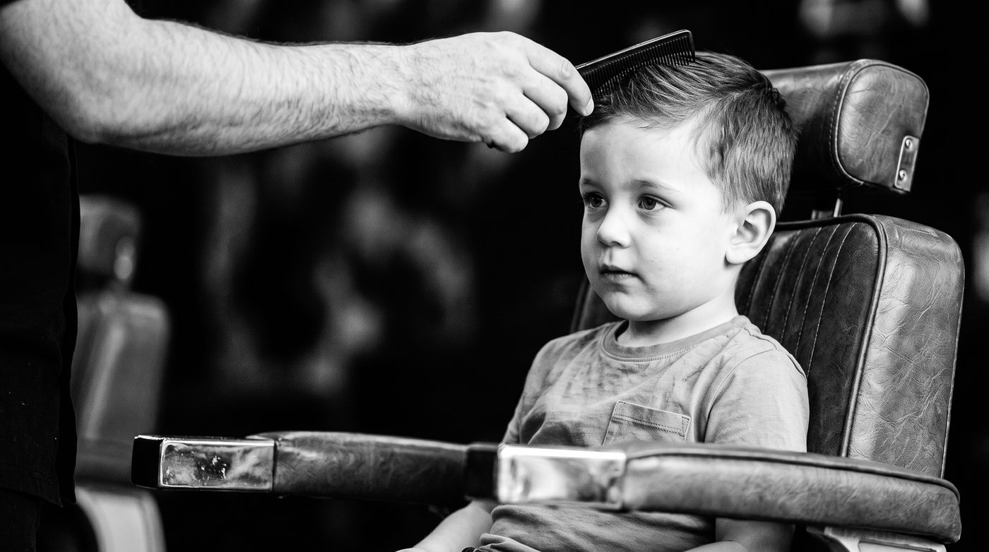 A barber gently combing the hair of a young boy sitting calmly in the barber chair