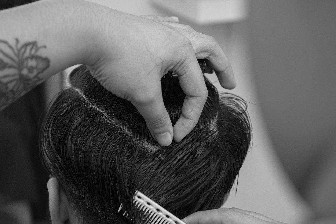 A barber lifting a section of hair between his fingers while cutting