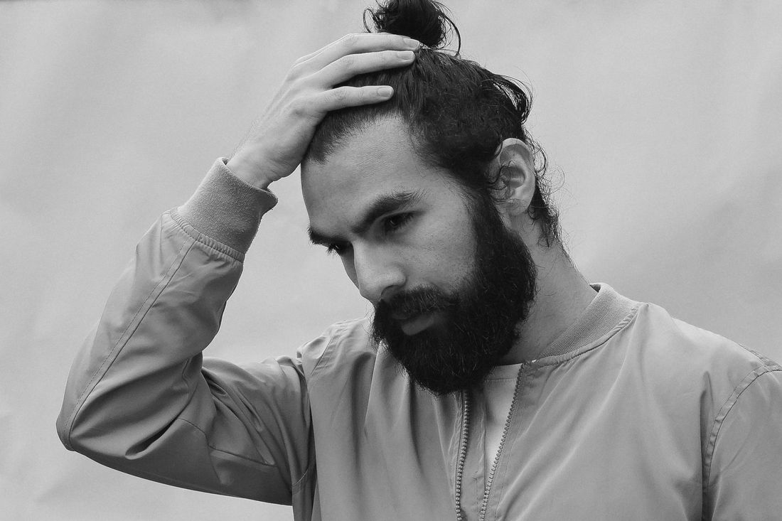 A man with a bun and a beard running a hand through his hair