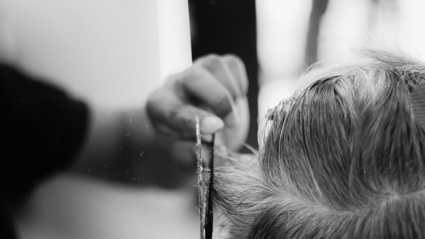 A barber cutting a client's thick gray hair with scissors