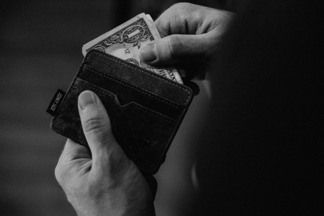 Hands pulling a dollar bill from a leather wallet