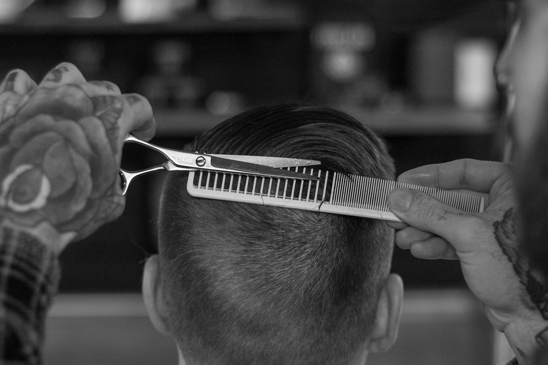 A barber cutting along a comb at the back of a client's head