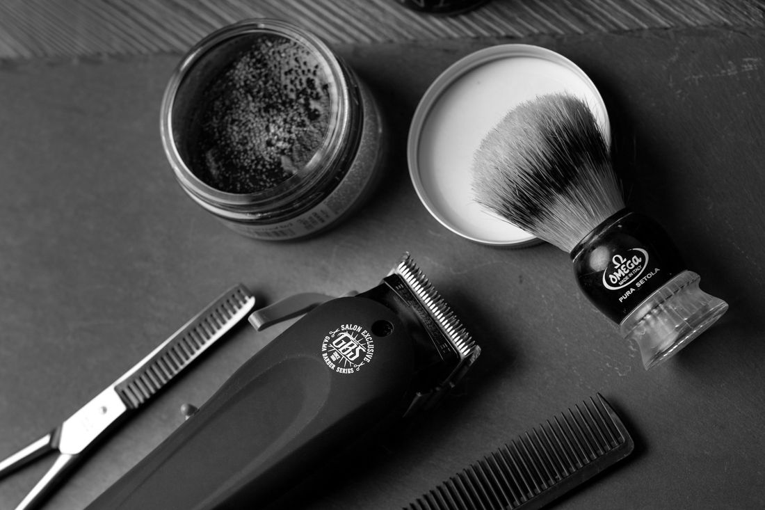 A small jar of grooming product beside a brush and comb on a dark surface