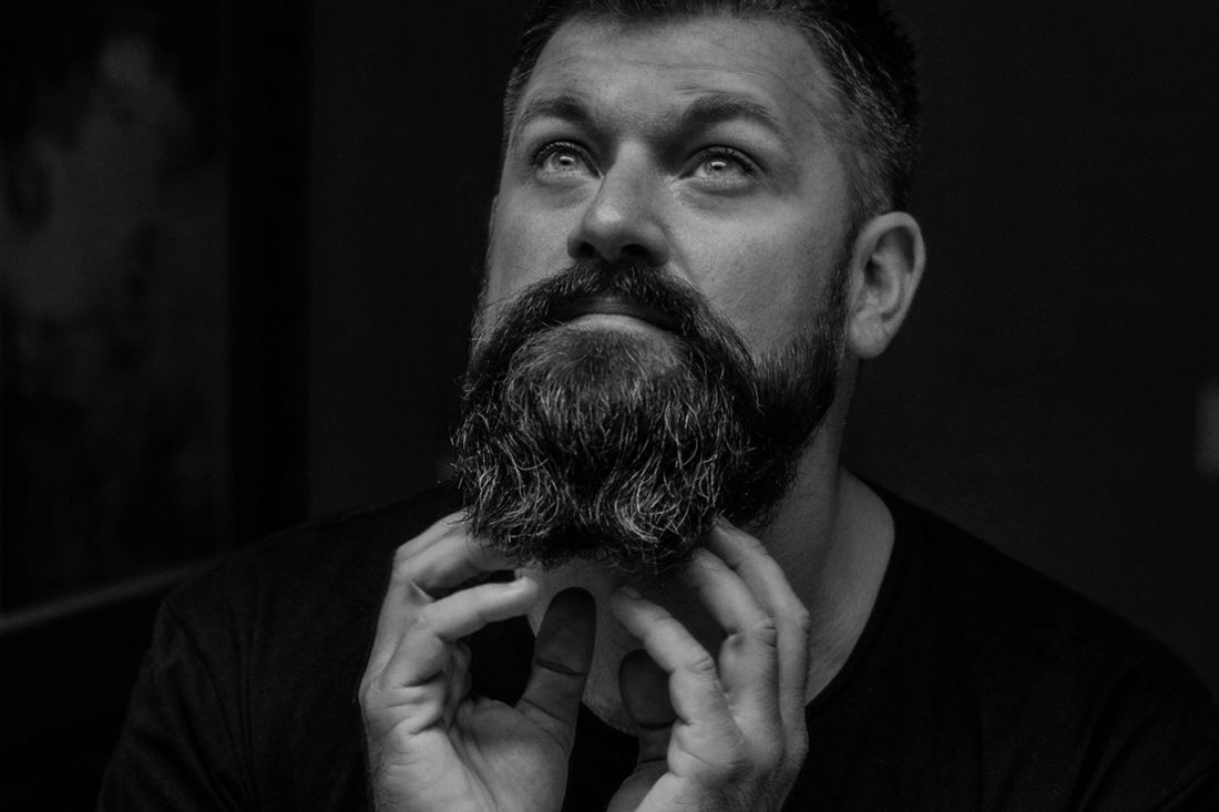 A bearded man looking upward with his hands near his chin