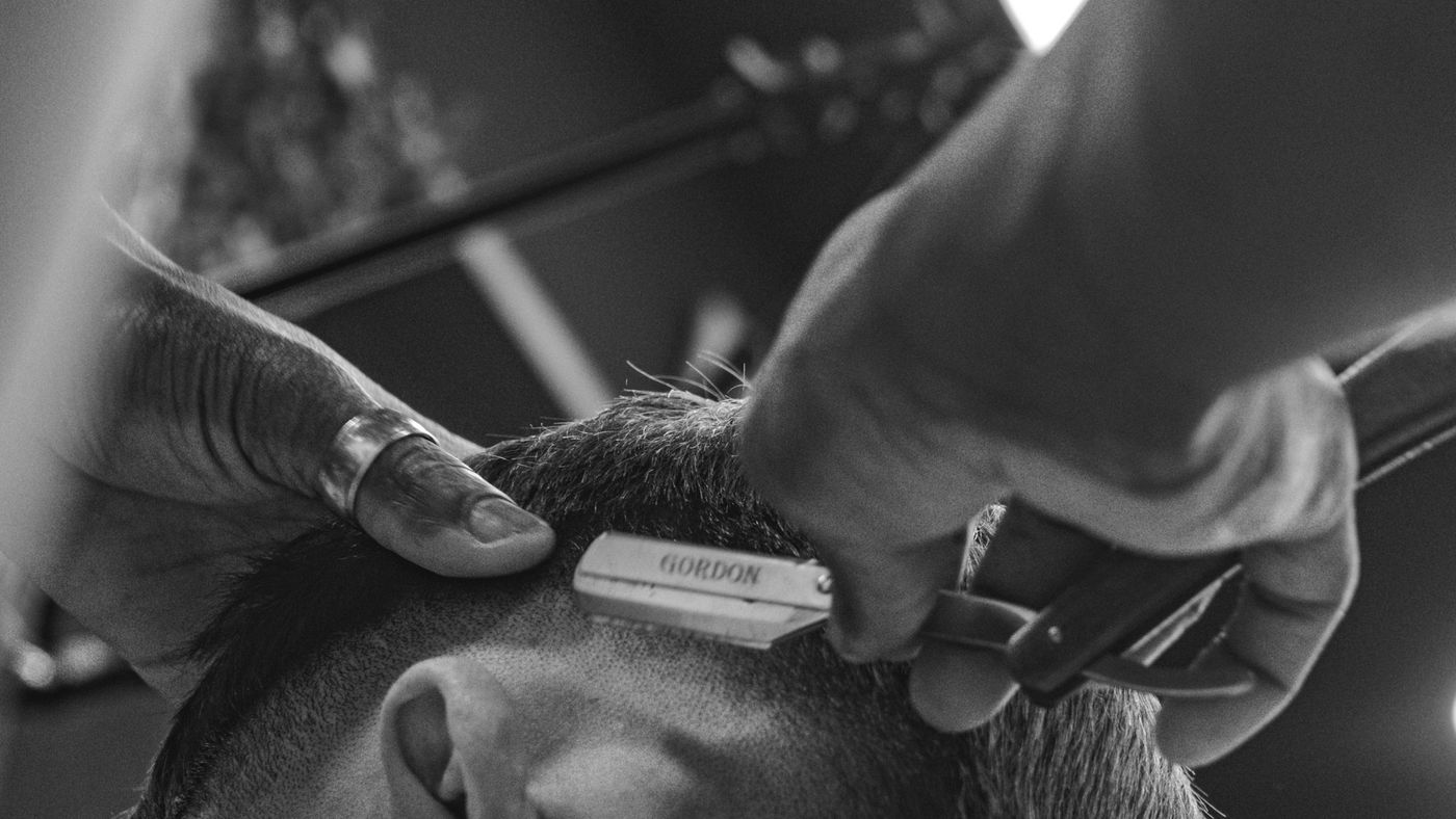 A barber carefully working close to a client's hairline in a barbershop