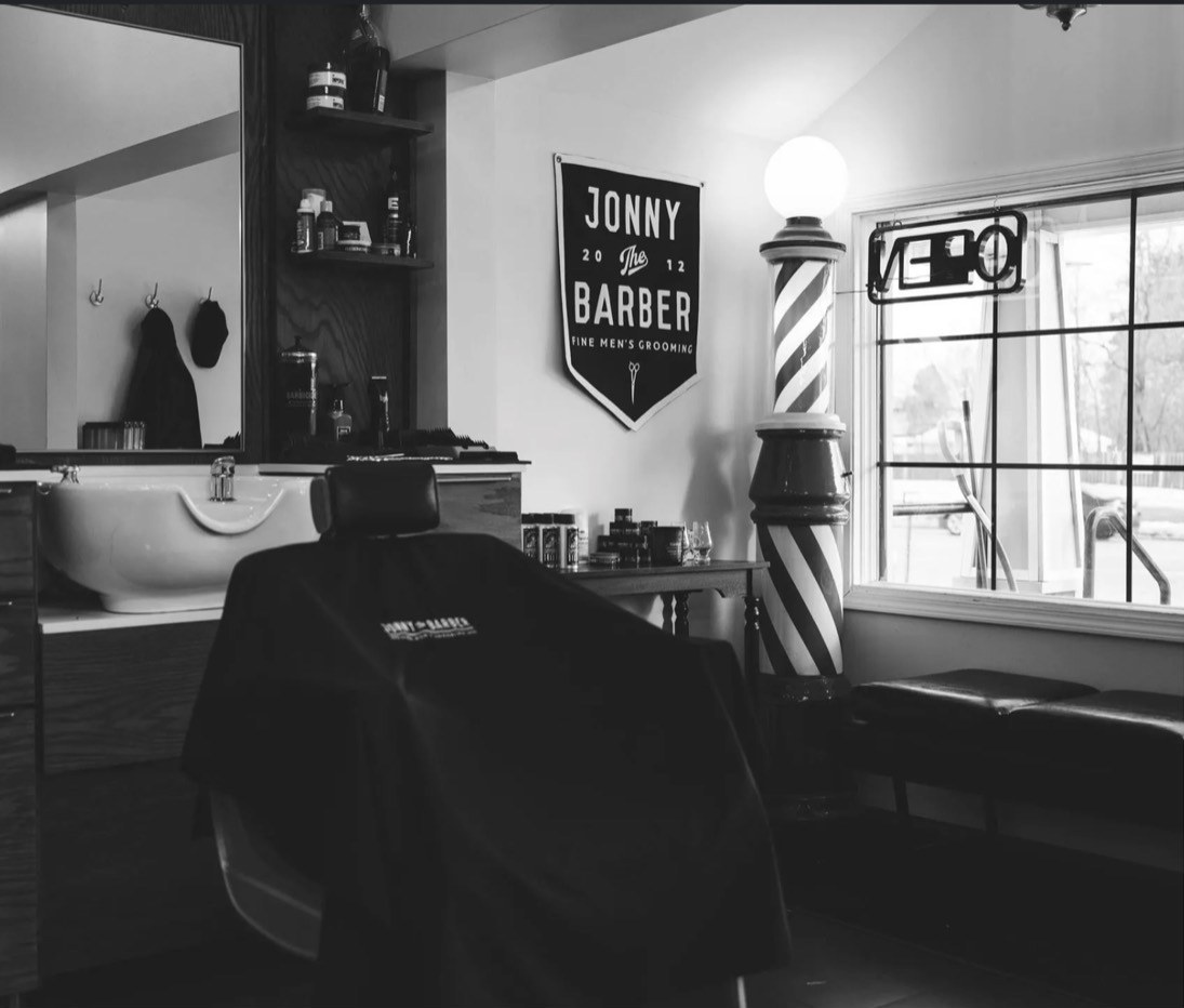 Inside Jonny the Barber Williamsville — barber pole, chair and neon Open sign